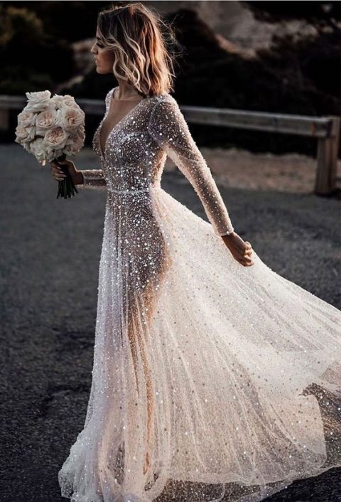 a fully embellished A-line see-through wedding dress with a covered plunging neckline and long sleeves