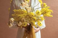 a bold yellow wedding bouquet composed of various types of flowers and decorated with long yellow ribbons