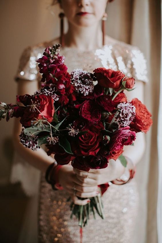 a deep red wedding bouquet with some dark carnations and foliage looks decadent and very chic