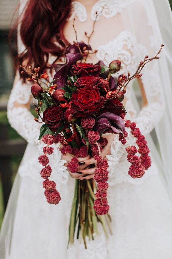 a deep red wedding bouquet with touches of purple and cascading elements okus blooming branches is elegant and decadent
