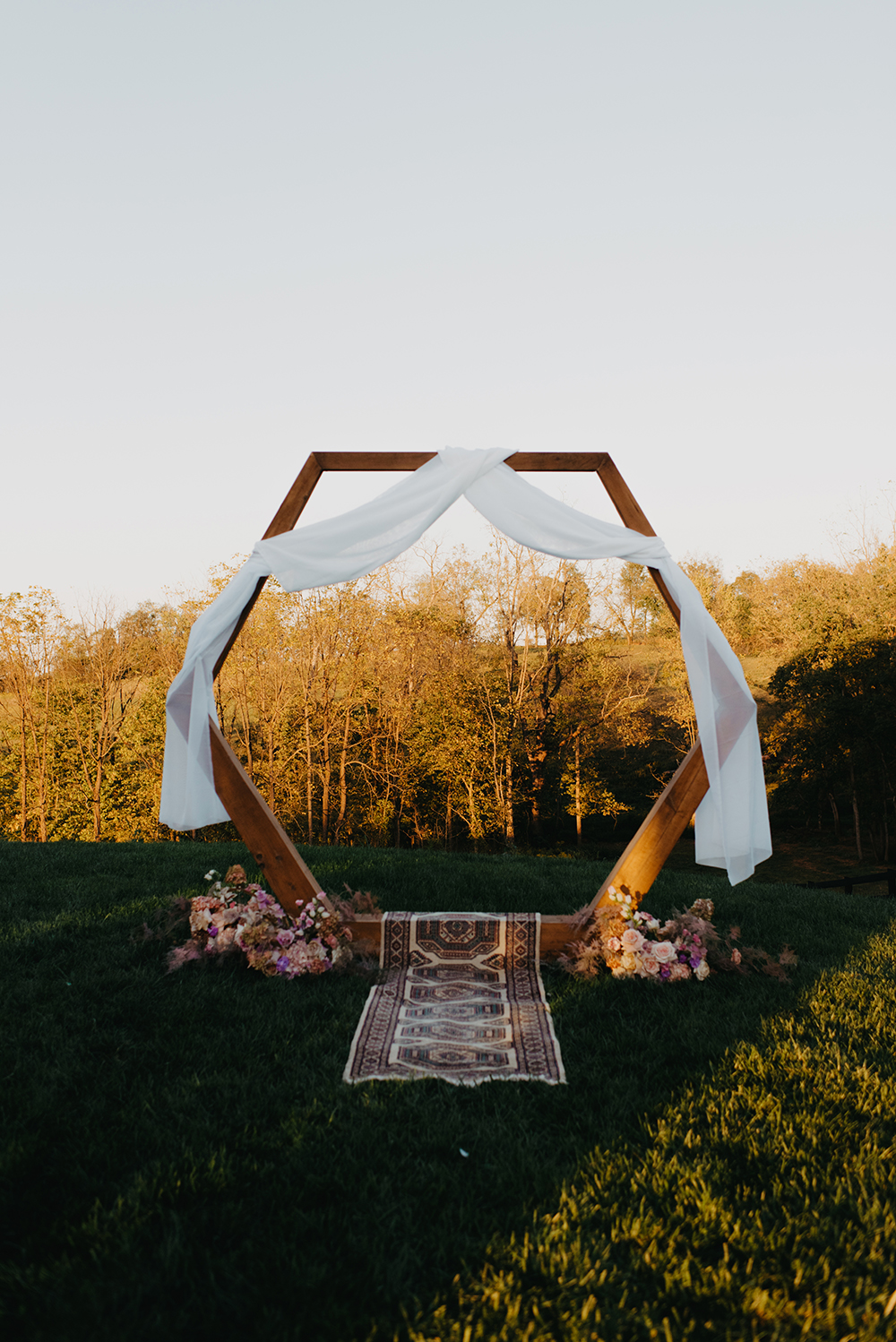 The wedding arch was done with white fabric, lush blooms and a boho rug