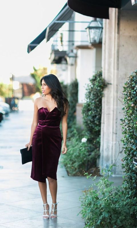 a deep purple strapless knee velvet dress with an asymmetrical neckline, a black clutch and silver heels for a sexy look