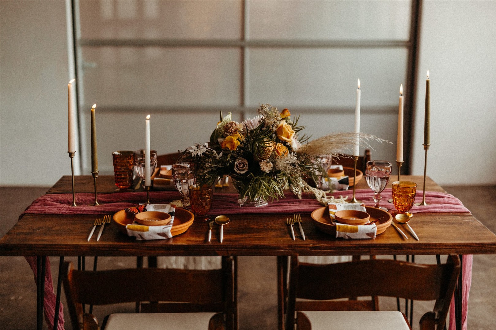The wedding tablescape was done with a pink table runner, tall candles, a bold floral centerpiece and terra cotta plates