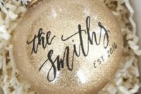 11 a gold glitter Christmas ornament with the name done in calligraphy is a stylish option for a winter engaged couple