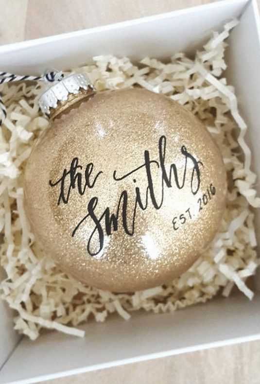 a gold glitter Christmas ornament with the name done in calligraphy is a stylish option for a winter engaged couple