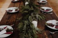 11 a simple evergreen table runner and white candles plus burgundy napkins and evergreens on each place setting