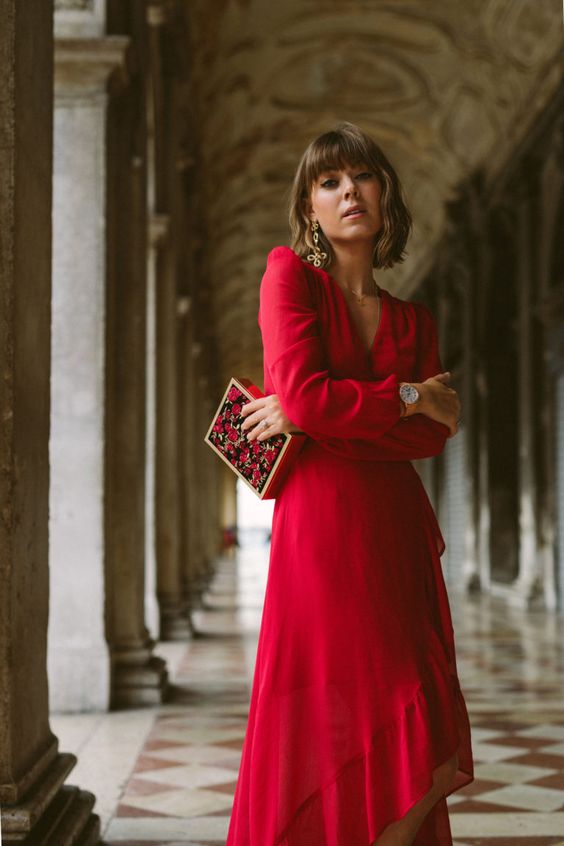 a red A line midi dress with an asymmetrical skirt, long sleeves, statement earrings and a bold floral box clutch