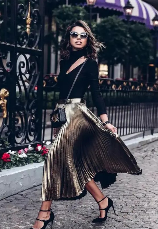 a black turtleneck top with a cutout, a metallic pleated skirt, black shoes and a small bag