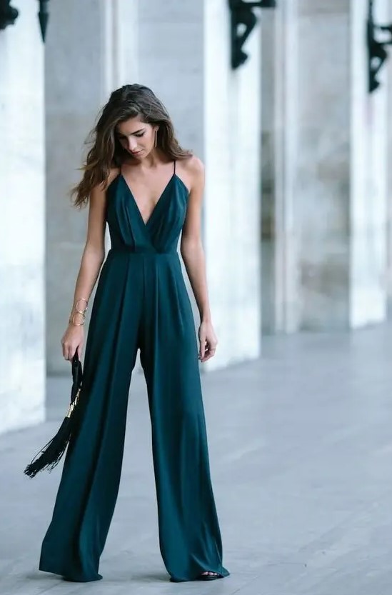 a dark green jumpsuit on spaghetti straps, with wideleg pants and a tassel clutch for a Christmas wedding