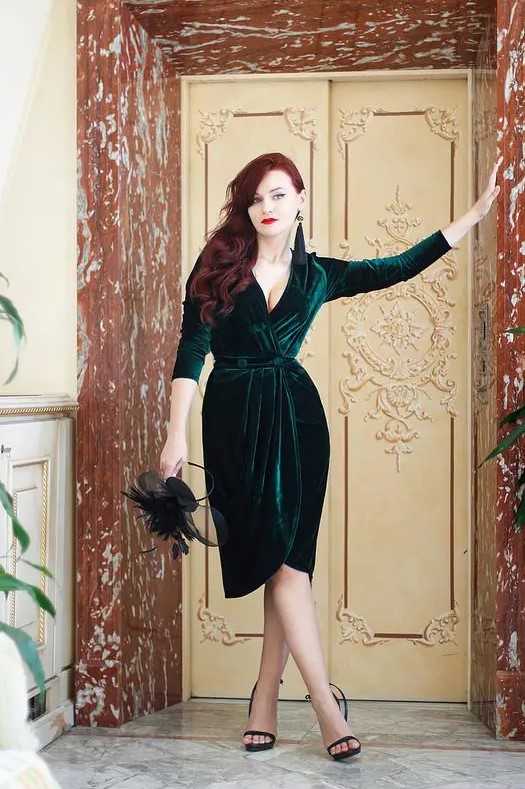 a gorgeous wrap emerald velvet dress with a plunging neckline, half sleeves, with buttons and black shoes and tassel earrings