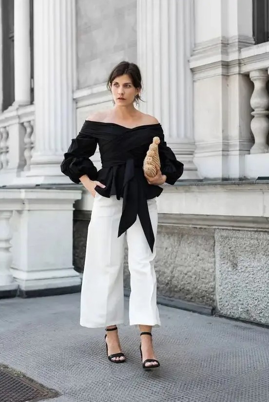 a monochromatic look with an off the shoulder black draped blouse, white wideleg pants, black heels and a woven clutch