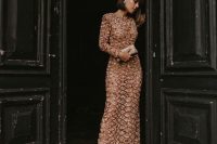 a nude maxi beaded and embroidered wedding guest dress with long sleeves and a metallic clutch