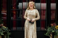 a shiny NYE wedding guest outfit with a gold sequin midi dress with long sleeves, black shoes and a small black clutch