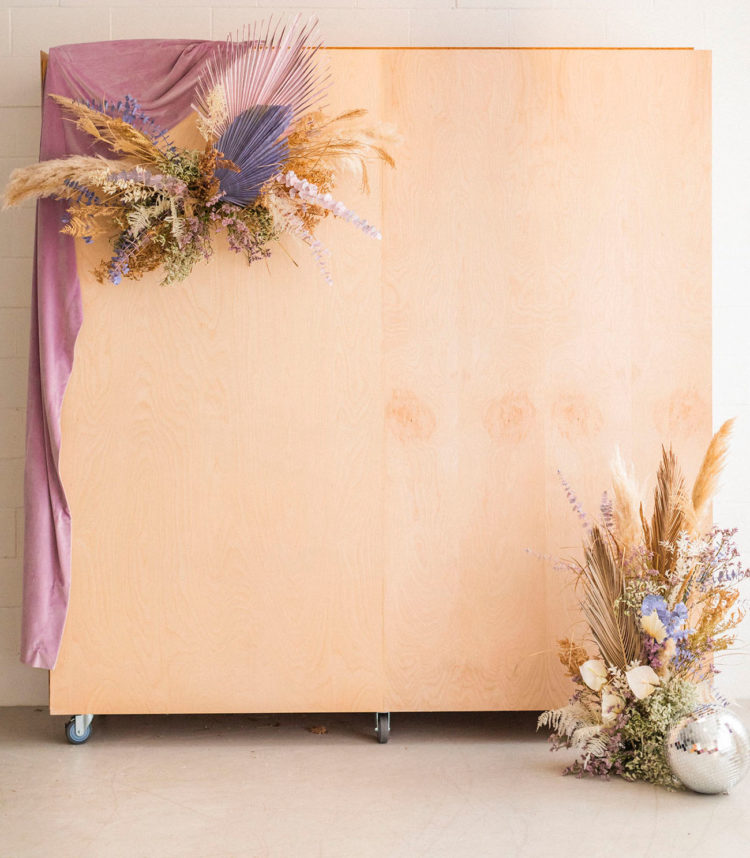 The wedding backdrop was done of plywood, with colored fronds, dried blooms and greenery