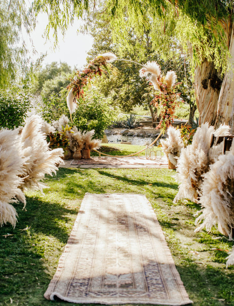 The wedding ceremony space was done with boho rugs, lots of pampas grass and a round arch with lush blooms and pampas grass