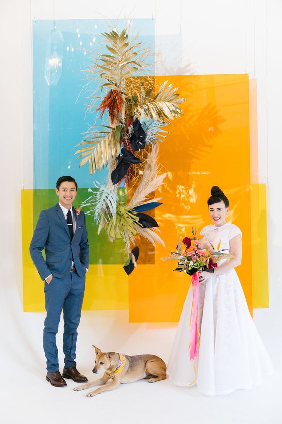 a crazy and bright color block wedding backdrop done with dried fronds, pampas grass and dark blooms