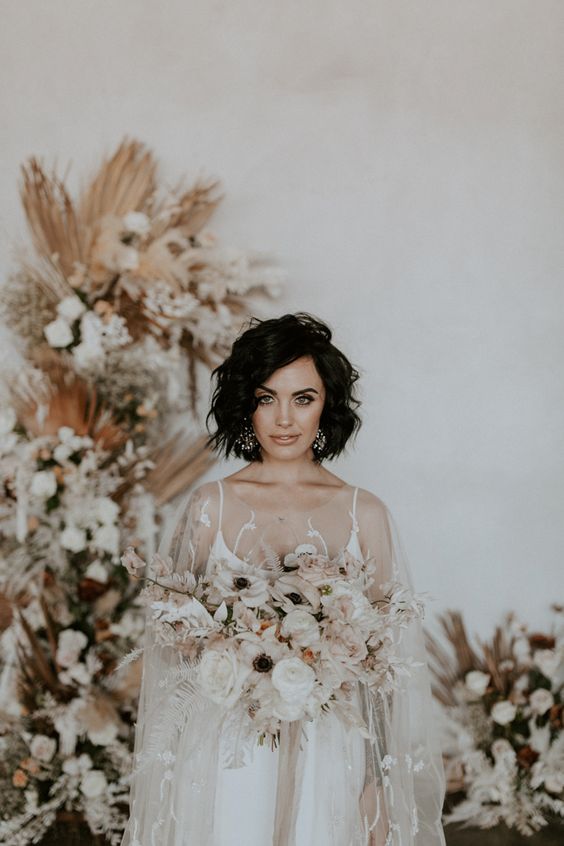 a neutral wedding ceremony space with dried and fresh neutral blooms, the bride in white and a cool and chic neutral bouquet