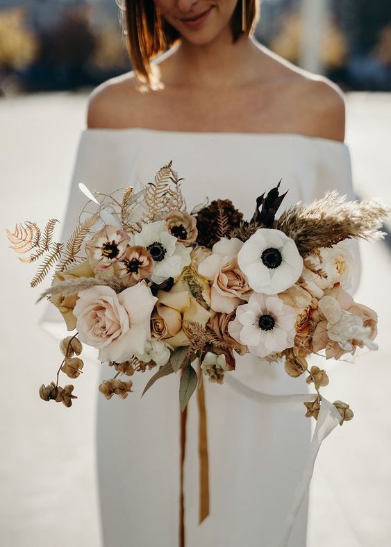 a chic wedding bouquet of white anemones, blush and dried roses, dried leaves, seed pods and dark foliage