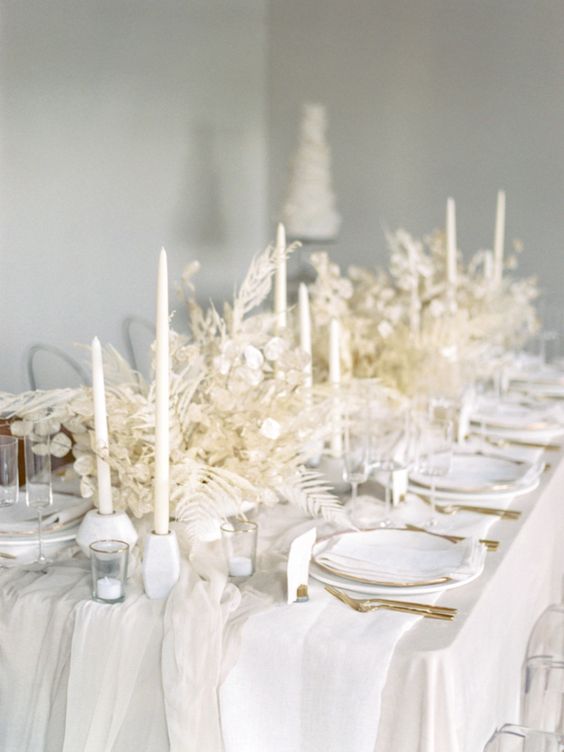 a refined white reception tablescape done with lunaria and dried branches, candles, plates and some gold cutlery