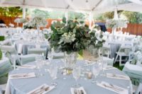 22 a pastel blue tablecloth and a greenery wedding centerpiece for a tender and refined wedding tablescape