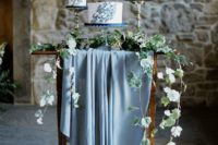 25 a sweets table with a pastel blue tablecloth, greenery and three wedding cakes with blue brushstrokes