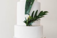 28 a white wedding cake decorated with tropical leaves and a single white bloom for a beach or tropical wedding