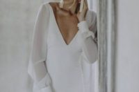 29 a modern and elegant wedding dress with a fitting silhouette, a plunging neckline, sheer long sleeves and tassel earrings