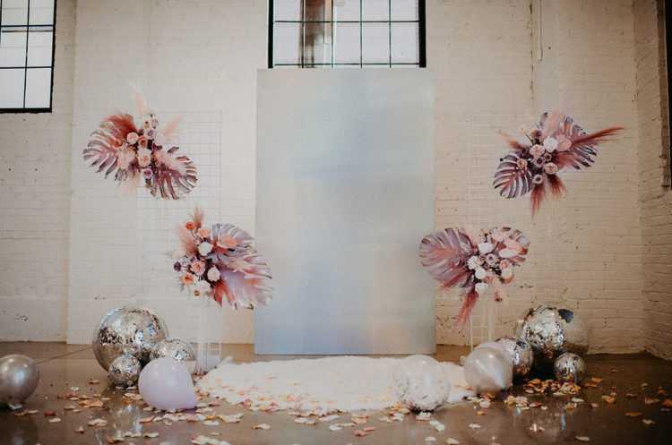 The wedding ceremony is fantastic, with pink palm leaves and blooms, silver disco balls, petals and a holographic backdrop