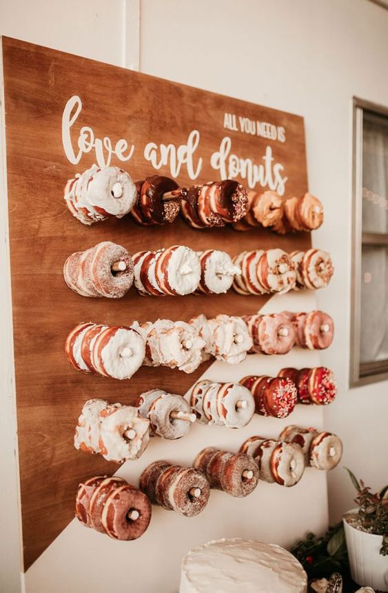 a mini glazed donut wall with white calligraphy is a cool idea to complete your dessert table