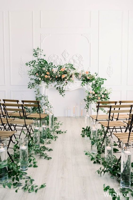 a gorgeous wedding ceremony space with greenery on the aisle and greenery and blooms on the faux mantel