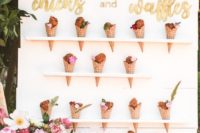 10 an ice cream cone wall with mini shelves, gold calligraphy and soem bright blooms and greenery in a vase