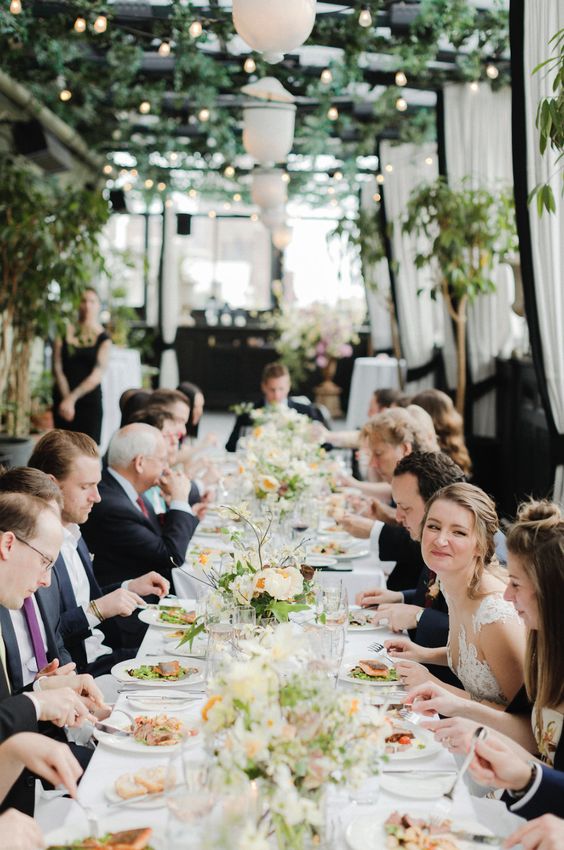 a cheerful and cool micro summer wedding reception with lush blooms and greenery and lights over it