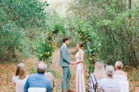 a small outdoor wedding ceremony space with a fall floral arch and greenery and just several guests