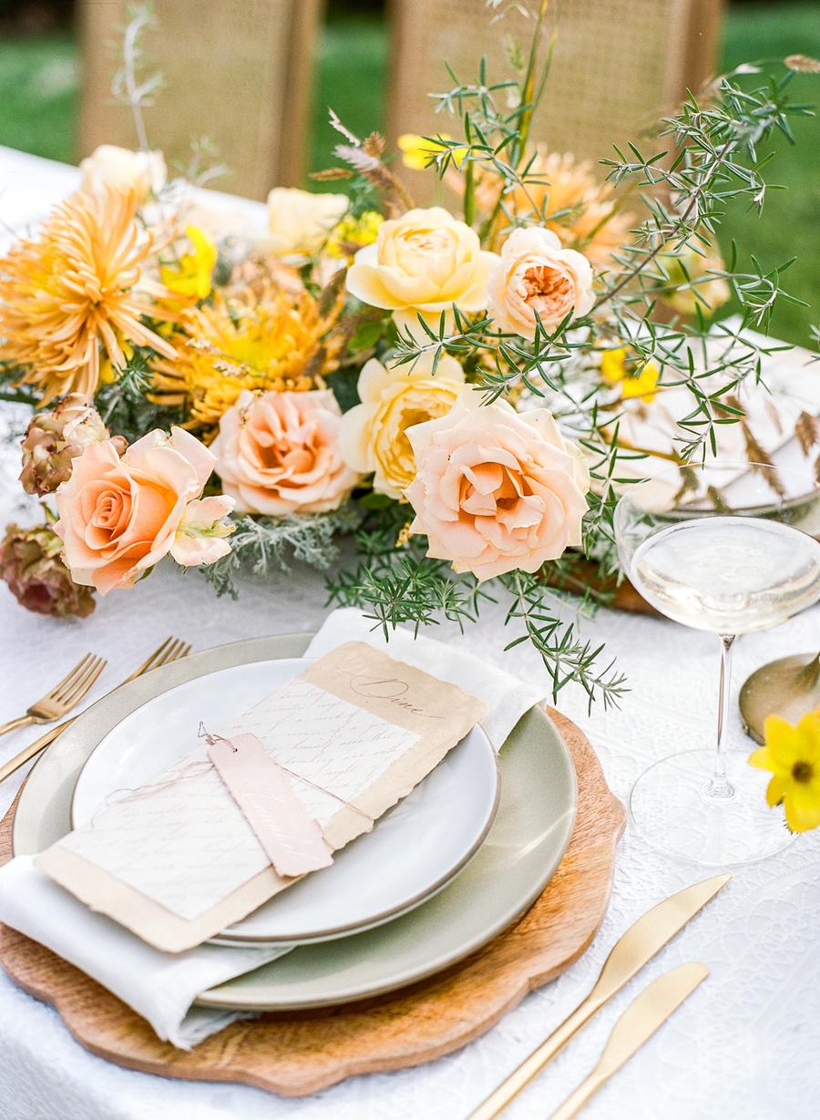 The wedding tablescape was done with a wooden charger, pastel plates and bright blooms and greenery