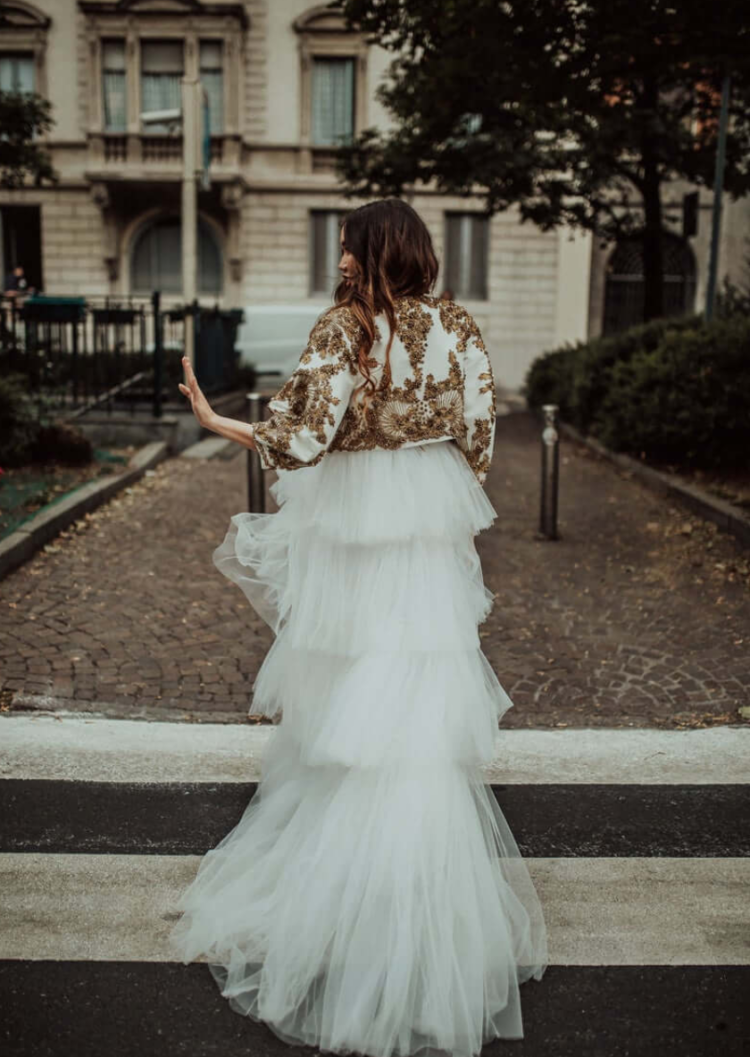 a gorgeous tiered tulle wedding dress with a train and a white cropped jacket with gold embroidery to cover up for a high fashion look