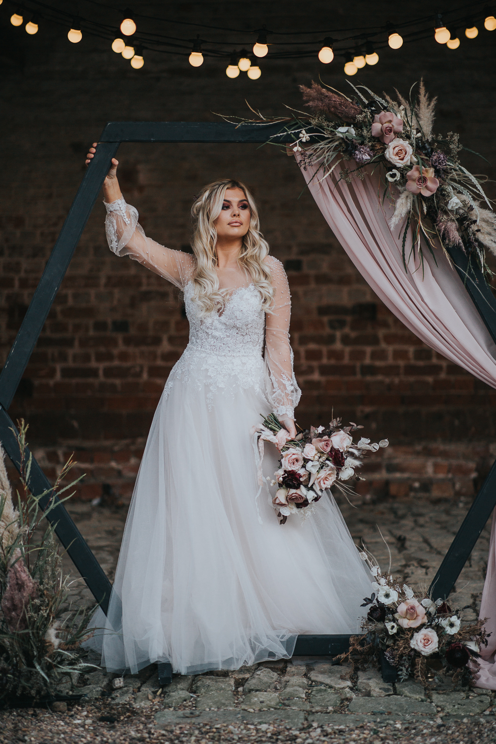 A black hex wedding arch was decorated with blush and mauve blooms, pampas grass and greenery