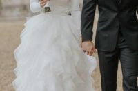 13 a modern wedding dress with a sleek and plain bodice with long sleeves and a tiered tulle skirt with a small train