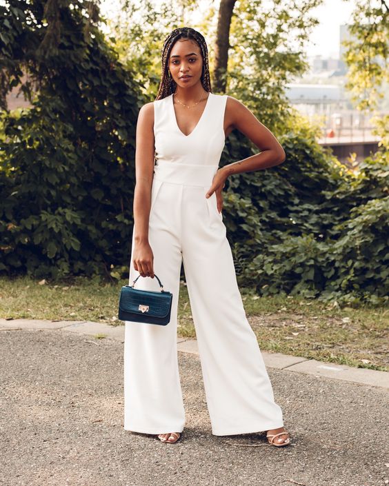 A chic and cool white jumpsuit with a V neckline, no sleeves, wideleg pants, nude shoes and a small black bag