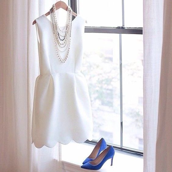 a modern plain sleeveless wedding dress with a high neckline and a scallop edge is completed with blue heels and statement necklaces