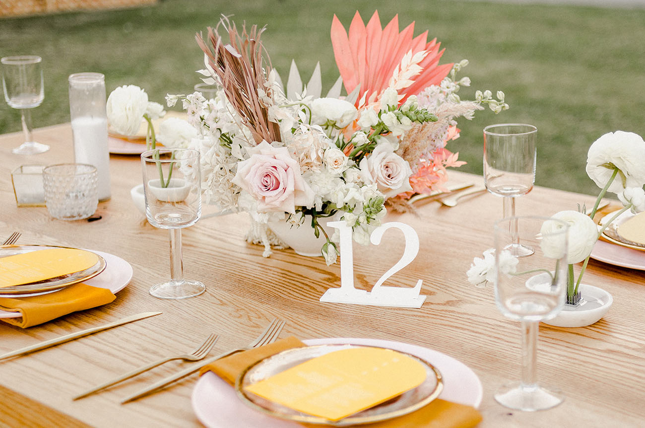 The wedding tablescape was done with blush blooms, pink fronds and mustard napkins