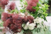 a beautiful wedding arrangement with burgundy smoke bush, dark leaves, greenery and white blooms looks refined