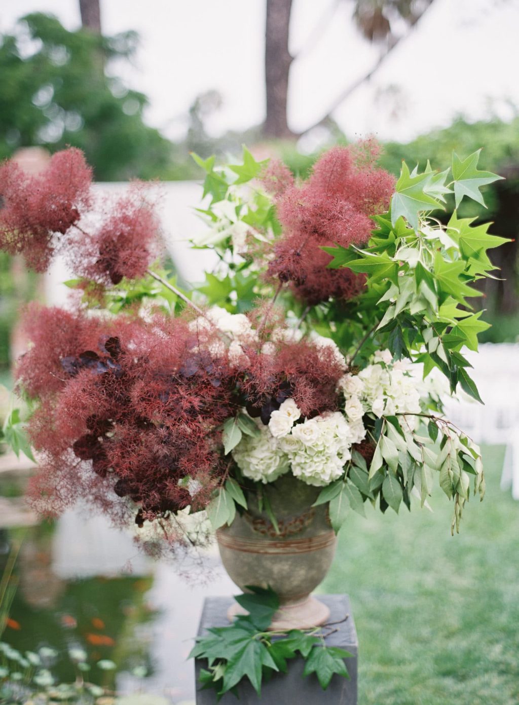 A beautiful wedding arrangement with burgundy smoke bush, dark leaves, greenery and white blooms looks refined
