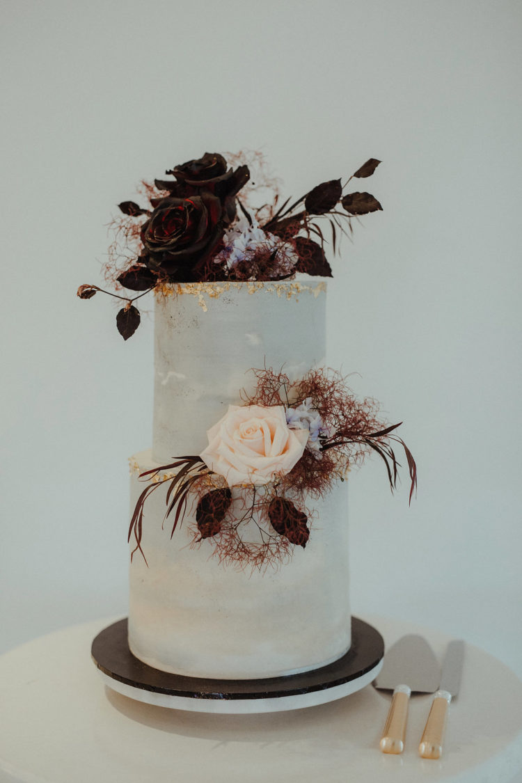 a chic wedding cake with gold leaf, dark and blush roses, leaves and smoke bush looks really unusual