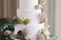 a delicate wedding cake in white decorated with green blooms and burgundy smoke bush