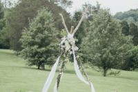 02 a boho wedding arch – a teepee with white fabric, greenery and white blooms, with florals and candle lanterns around