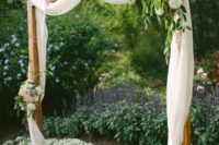 04 a romantic backyard wedding arch of wood, with airy white fabric and light pink and white blooms and greenery