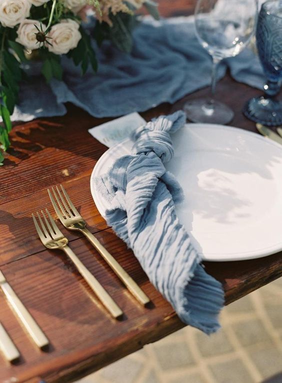 a blue gauze table runner and a matching napkin for a beautiful and ethereal wedding tablescape
