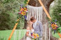 09 a triangle wedding arch with long fringe, greenery and bright blooms is ideal for a boho backyard wedding