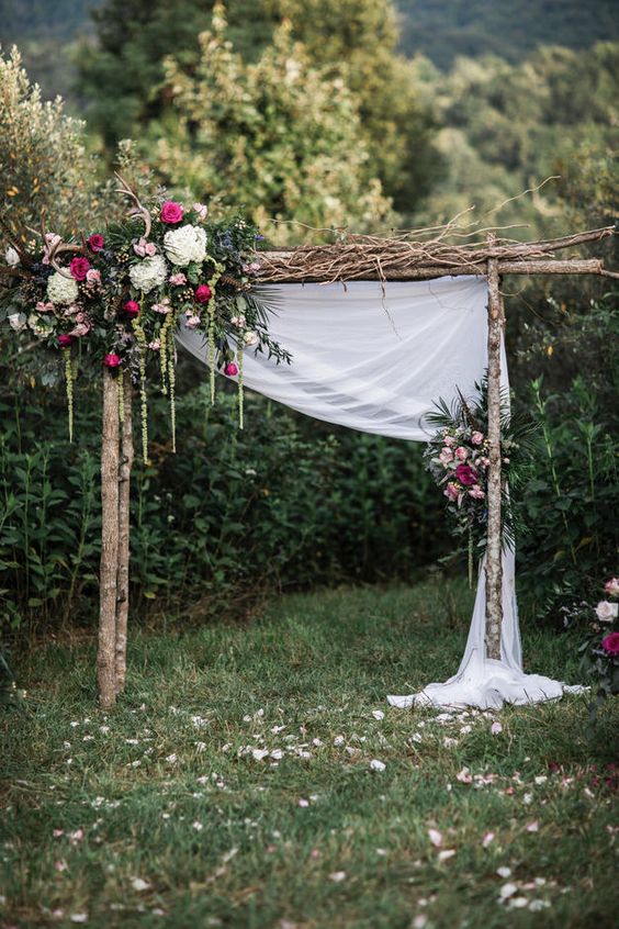 a whimsy backyard wedding arch of branches and sprigs, lush jewel tone florals, greenery and antlers for a boho fall wedding