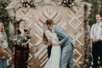 17 a boho backyard wedding backdrop of plywood, with geometric decorative patterns and some white florals and pampas grass on top